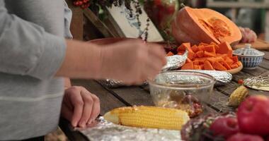 Female hands with spoon add sauce to corn cob and thyme, then wrap corn cob in foil before grill. Closeup hands put seasonings and dried herbs to yellow sweet corn. Preparing vegetables for bbq grill video