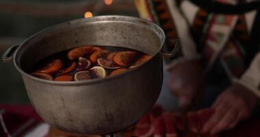 Cooking traditional drink from red wine and citrus for Christmas. Hands cut grapefruit and put red citrus slices into cauldron of mulled wine. Holiday gluhwein preparation with blurry background video