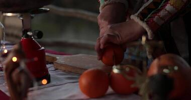 Hands slicing fresh orange on wooden cutting board. Cooking in Christmas time. Person cut orange citrus fruit in halves, then in semicircular slices. Blur golden blinking lights on foreground, low key video