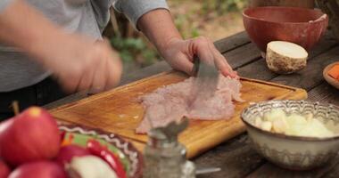 Female chef hands tenderize turkey fillet meat by beating with meat tenderizer. Cooking of fresh raw turkey breast on wooden cutting board at rustic table with traditional crockery and fall vegetables video