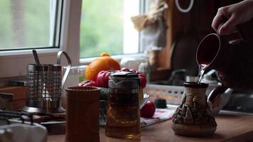 Hands make coffee in ceramic cezve on kitchen table near window for morning drinks. Person pour water from rustic clay jug into cezve of coffee video
