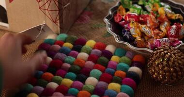 Hand touch colorful felt hot stand. Warm Christmas gathering unfolds with vibrant candies displayed on table adorned with holiday decor. Atmosphere is inviting, filled with joy and festive spirit. video