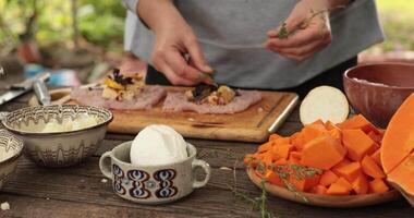 Female hands add thyme leaves atop cheese and roll into turkey cops to make roulades for thanksgiving day. Cooking of stuffed turkey rolls for Thanksgiving dinner on rustic table with ceramic crockery video