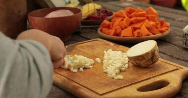 POV female hands chop raw celery root for cooking, cut into small cube pieces with knife. Cooking healthy meal from fall vegetables at rustic wooden cutting board. Preparation healthy food ingredients video