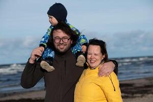 A happy family strolls along a chilly autumn beach, with their young son joyfully running ahead, creating lasting memories as the crisp wind and soothing waves embrace them in a moment of pure photo