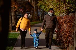 A loving couple strolls through a sunlit park with their young son, surrounded by the vibrant colors of autumn, enjoying a joyful and peaceful family moment together. photo