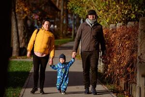 A loving couple strolls through a sunlit park with their young son, surrounded by the vibrant colors of autumn, enjoying a joyful and peaceful family moment together. photo