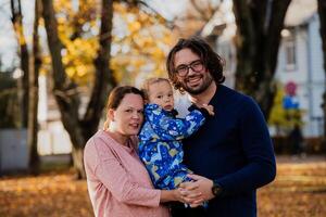 On a sunny autumn day in the park, a mother and father lovingly embrace their young son, sharing moments of laughter and joy as they play together photo