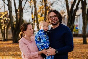 On a sunny autumn day in the park, a mother and father lovingly embrace their young son, sharing moments of laughter and joy as they play together photo