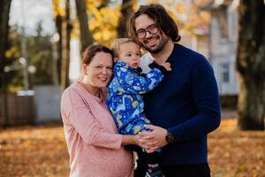 On a sunny autumn day in the park, a mother and father lovingly embrace their young son, sharing moments of laughter and joy as they play together photo