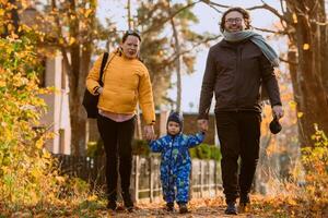 A loving couple strolls through a sunlit park with their young son, surrounded by the vibrant colors of autumn, enjoying a joyful and peaceful family moment together. photo