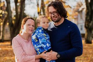 On a sunny autumn day in the park, a mother and father lovingly embrace their young son, sharing moments of laughter and joy as they play together photo