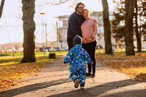 A loving couple strolls through a sunlit park with their young son, surrounded by the vibrant colors of autumn, enjoying a joyful and peaceful family moment together. photo