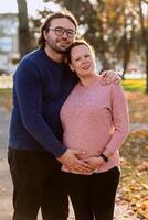 A man lovingly embraces his pregnant wife in the park, sharing a peaceful moment of warmth and affection photo