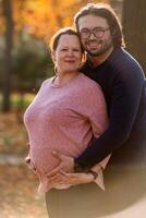 A man lovingly embraces his pregnant wife in the park, sharing a peaceful moment of warmth and affection photo