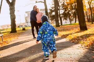 A joyful little boy in his winter coat and hat plays happily in the park, surrounded by the love and warmth of his smiling parents photo