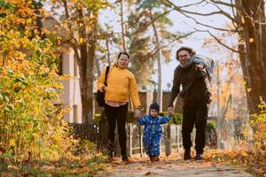 A loving couple strolls through a sunlit park with their young son, surrounded by the vibrant colors of autumn, enjoying a joyful and peaceful family moment together. photo