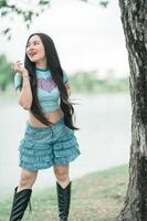 A woman in a blue shirt and denim shorts standing next to a tree photo