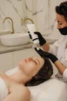 Close-up of the beautician's hands applying cream to the client's face and doing a massage. Facial skin care. Vertical photo