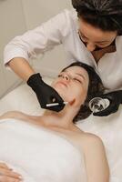 The cosmetologist applies a liquid gel to the face with a wide brush, the carboxytherapy procedure and its preparations. photo