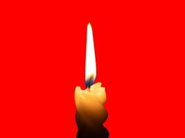 A single burning candle flame or light glowing on a small spiral yellow candle isolated on red background with clipping path photo