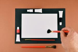 A person holding a brush and a piece of paper next to a box of paint photo