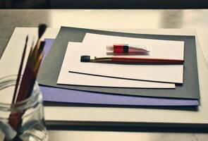 A table with a paintbrush, paper, and a jar photo
