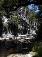 Shaded Stream flows in front of Rock wall photo
