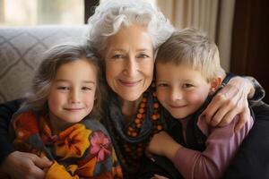 happy caucasian grandmother hugs grandchildren boy and girl, all looking at camera and smiling. photo from inside the house