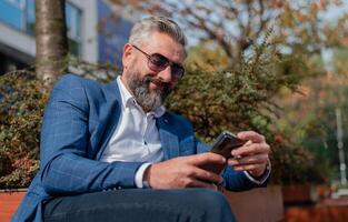 A happy handsome business man using mobile phone app texting while sitting on the park bench. photo