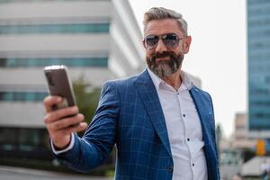 A happy mature business man using a cell phone app texting outside of the office in the city with urban buildings in the background. photo