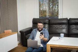 Angry stressed man yelling on his phone call with a burnout face expression while working at the home office. photo