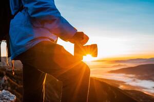 A male photographer taking a photo on the mountain top at sunrise or sunset adventure travel photography.