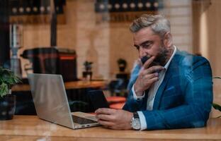 A thoughtful worried mature business man thinking of problem solution while working on a laptop in the office near the window. photo