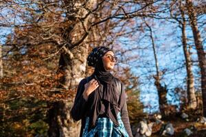 A happy woman in hijab enjoying in nature while walking in the autumn forest. photo