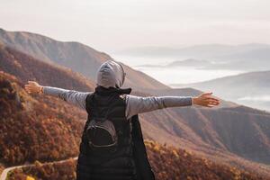 A woman who hikers enjoys a break look at the top of the mountain with hands open. Adventure travel. Concept of success free freedom happy new life. photo