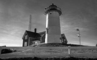 Lighthouse Tower Standing Tall Against a Cloudy Sky with Surrounding Grass and Plants photo