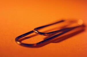 Close-Up of a Single Paperclip on Orange Background photo