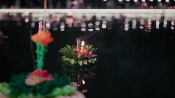 A delicate krathong adorned with vibrant flowers and a flickering candle floats serenely on the water, symbolizing hope and gratitude during the enchanting Loy Krathong festival in Thailand. video