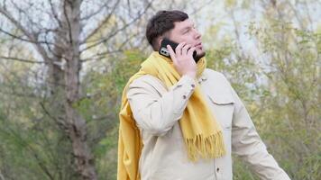 young caucasian man walking in the park and using smartphone, having a call video