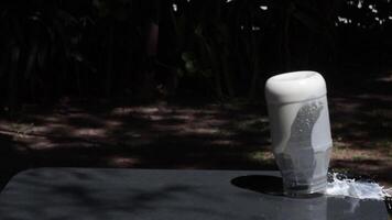 Slow motion capture of a jar filled with milk tipping over in a garden setting video