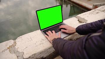 Man in mask works on laptop with chromakey screen on bridge video