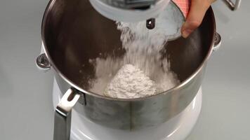 Woman pours flour into large bowl of dough maker with butter video