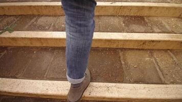 Man in coat jeans and grey shoes goes up bridge stone steps video