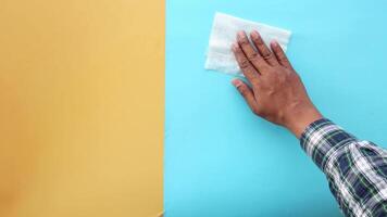An individual is focused on cleaning a blue surface using a wipe, set against a yellow background video