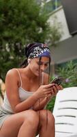 A young woman is happily engaged with her smartphone while enjoying a peaceful outdoor setting video