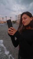 A Young Woman Relaxes and Enjoys the Beautiful Sunset at the Beach While Using a Smartphone video