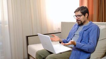 man in online conference is angry and shouts while sitting at the table in the bedroom at home, looking at the laptop. video