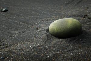 Smooth green stone on a black sand beach photo