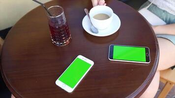 A woman is sitting at a table with a green screen, ideal for app design, digital content creation, and product mockup presentations. video